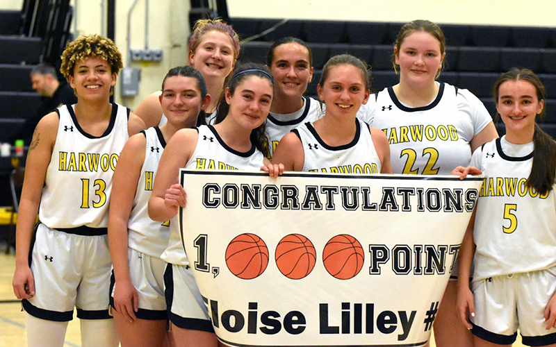 Harwood senior Eloise Lilley broke the 1000-point barrier on January 21, 2025, against Lake Region. Left-to-right are: Cheyenne Keller (13), Ava Reagan, Isabella Pockoski (tall in back), Briley Rutledge (holding sign next to EL), Roanha Chalmers, Eloise Lilley, Kendra Rocheleau (22), Maddie Ryley (5).